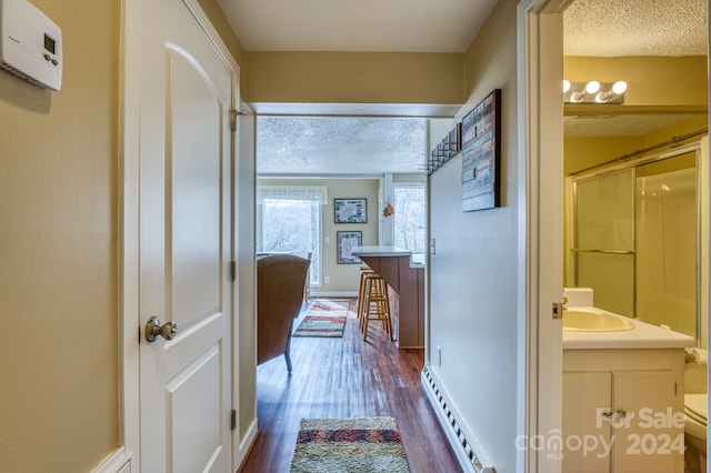 hallway featuring dark hardwood / wood-style flooring, a textured ceiling, a baseboard radiator, and sink