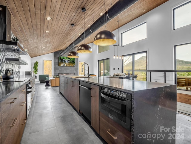 kitchen with light tile flooring, hanging light fixtures, an island with sink, sink, and wooden ceiling