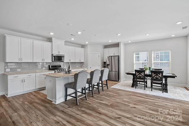 kitchen with backsplash, a kitchen island with sink, light wood-type flooring, white cabinets, and appliances with stainless steel finishes