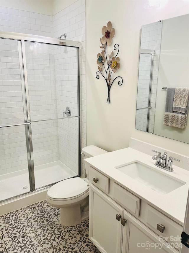 bathroom featuring tile patterned floors, vanity, toilet, and a shower with door