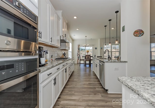 kitchen featuring sink, white cabinetry, light stone counters, hanging light fixtures, and backsplash