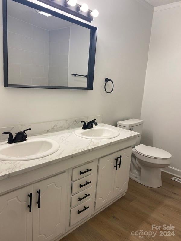 bathroom with dual vanity, ornamental molding, toilet, and wood-type flooring