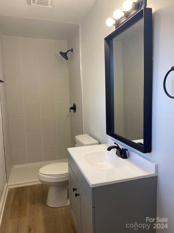 bathroom featuring wood-type flooring, tiled shower, a textured ceiling, toilet, and oversized vanity