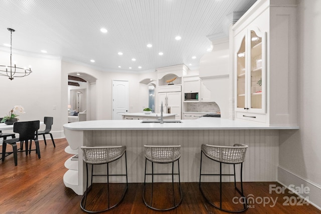 kitchen with built in appliances, a kitchen breakfast bar, white cabinetry, dark hardwood / wood-style floors, and tasteful backsplash