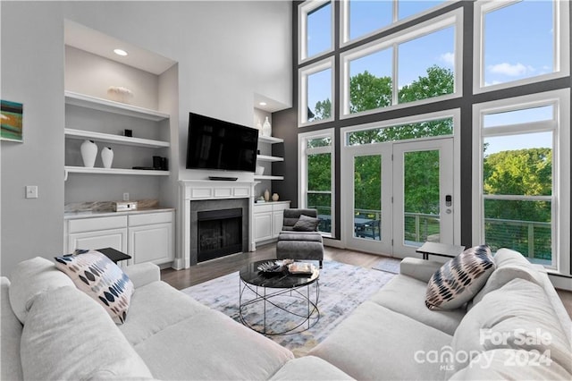 living room with a towering ceiling, light wood-type flooring, built in shelves, and a wealth of natural light