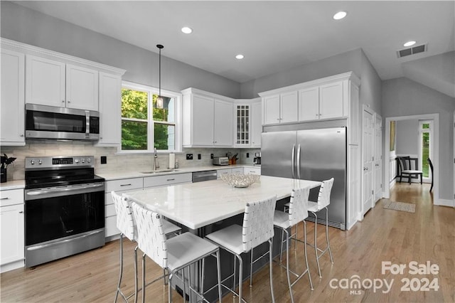 kitchen with appliances with stainless steel finishes, white cabinetry, a breakfast bar, and light hardwood / wood-style flooring