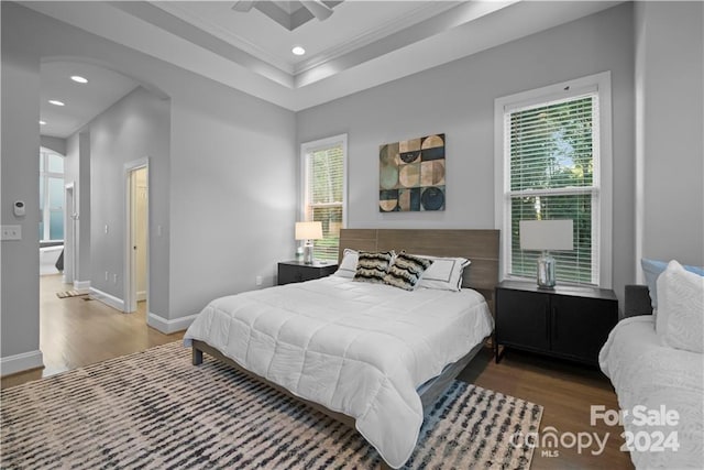 bedroom featuring ceiling fan, crown molding, dark hardwood / wood-style flooring, ensuite bathroom, and a tray ceiling