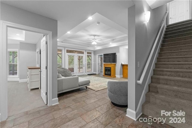 unfurnished living room with ceiling fan, plenty of natural light, a tray ceiling, and light tile floors