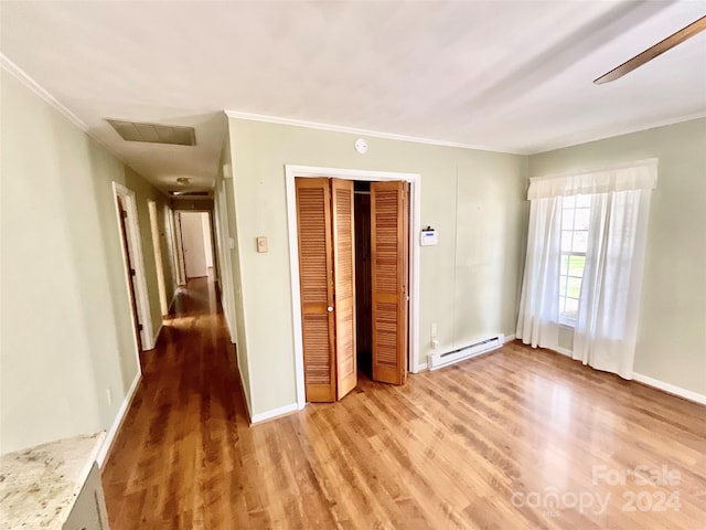 unfurnished bedroom featuring a closet, baseboard heating, wood-type flooring, and ceiling fan