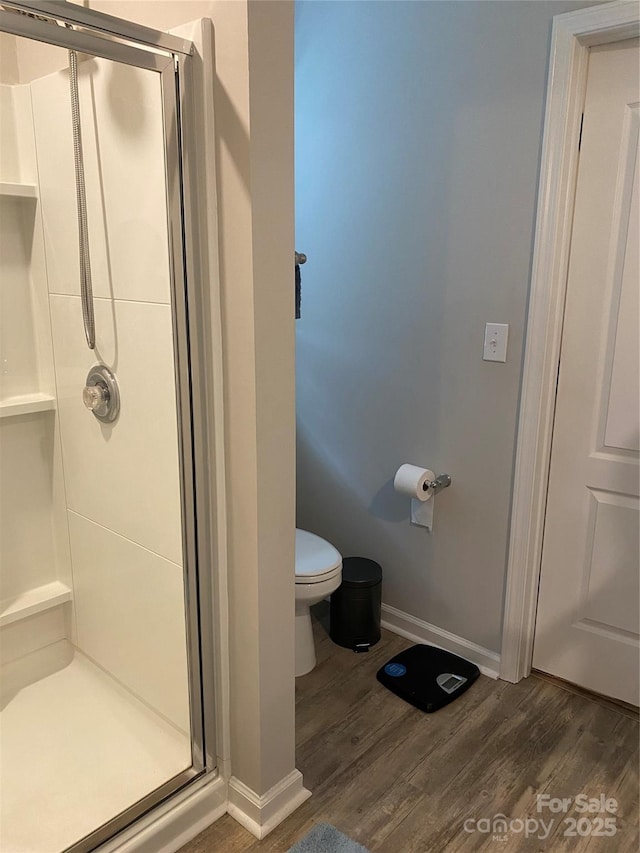 full bath featuring toilet, a stall shower, baseboards, and wood finished floors