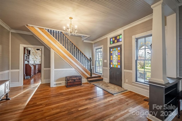 entryway with a chandelier, wood-type flooring, ornate columns, and ornamental molding