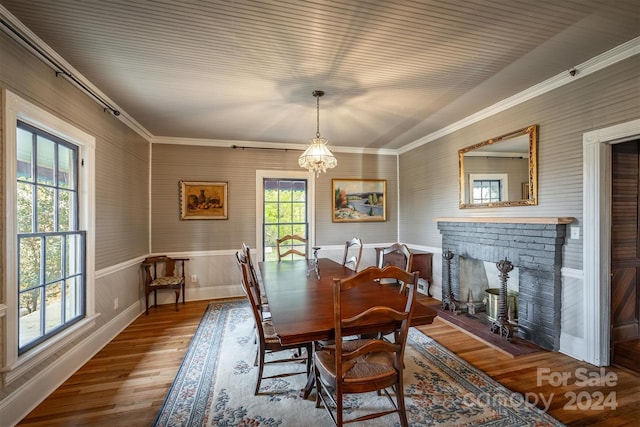 dining area featuring crown molding, a fireplace, hardwood / wood-style floors, and an inviting chandelier