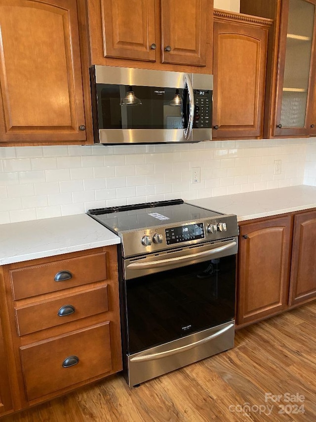 kitchen featuring tasteful backsplash, light hardwood / wood-style floors, stainless steel appliances, and light stone countertops