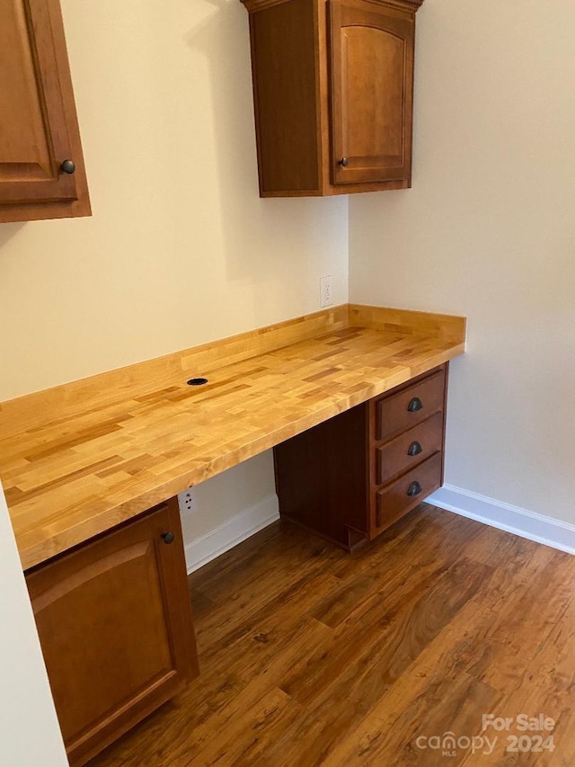 unfurnished office featuring dark hardwood / wood-style flooring and built in desk