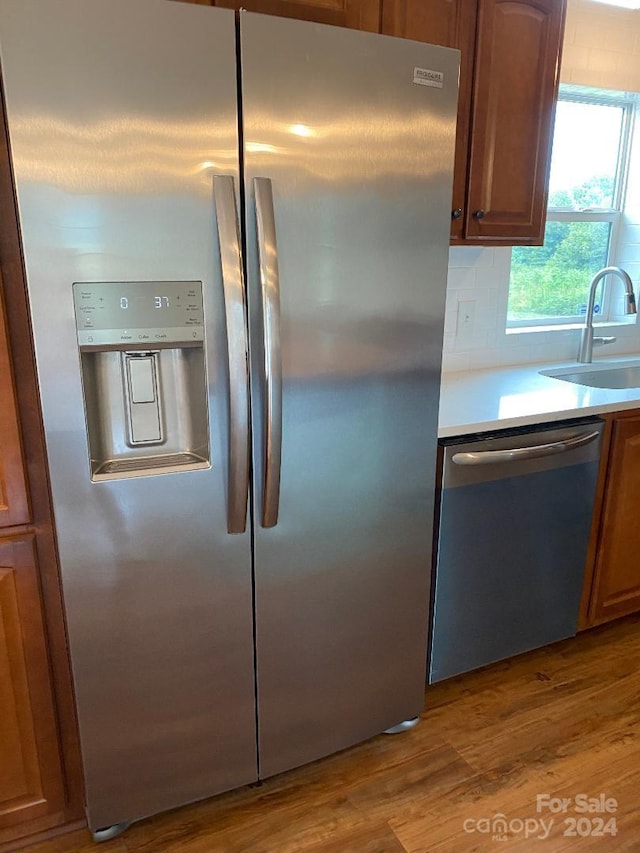 kitchen with appliances with stainless steel finishes, sink, backsplash, and hardwood / wood-style flooring