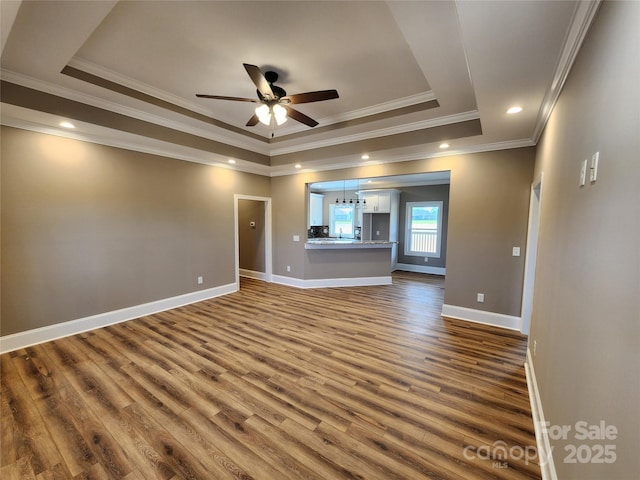 unfurnished living room with a tray ceiling, dark wood-style floors, baseboards, ceiling fan, and crown molding