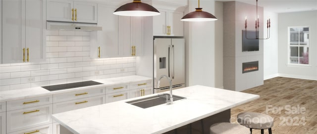 kitchen with high end fridge, hanging light fixtures, an island with sink, black electric cooktop, and decorative backsplash