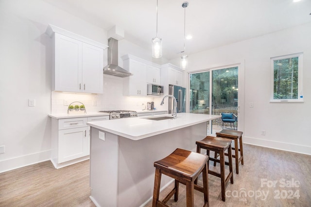 kitchen featuring white cabinetry, appliances with stainless steel finishes, hanging light fixtures, and wall chimney range hood