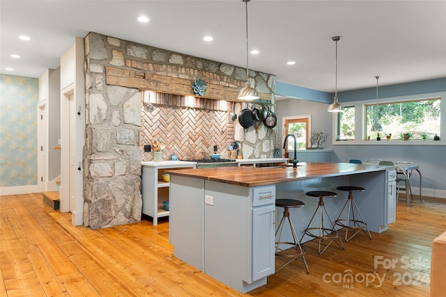 kitchen featuring light hardwood / wood-style flooring, a kitchen island with sink, butcher block counters, and hanging light fixtures