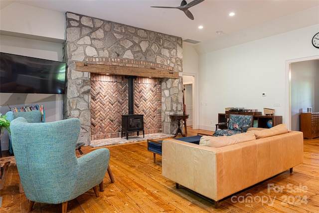 living room with ceiling fan, wood-type flooring, vaulted ceiling, and a wood stove