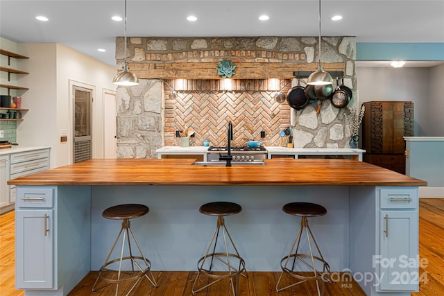 kitchen with a breakfast bar, a kitchen island with sink, pendant lighting, and light hardwood / wood-style floors