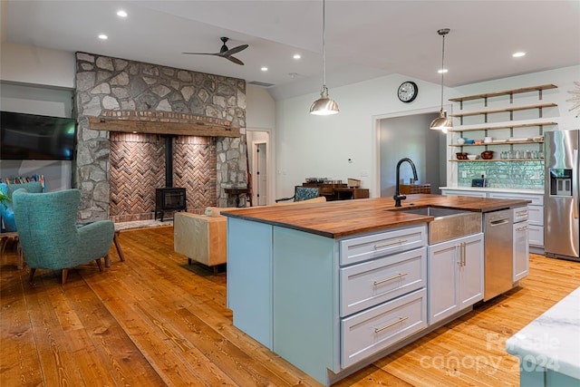 kitchen with a kitchen island with sink, stainless steel appliances, a wood stove, wood counters, and pendant lighting