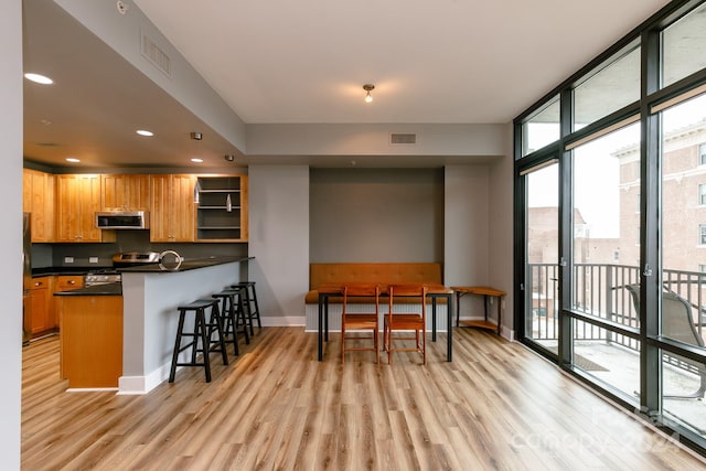 kitchen featuring floor to ceiling windows, a breakfast bar, kitchen peninsula, light wood-type flooring, and appliances with stainless steel finishes