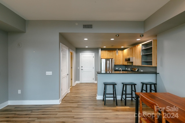 kitchen featuring a kitchen breakfast bar, stainless steel appliances, light hardwood / wood-style flooring, and kitchen peninsula