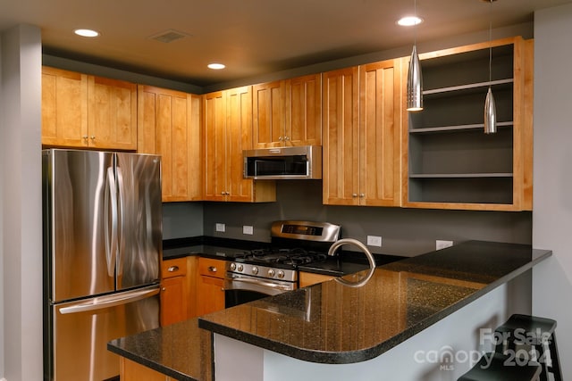 kitchen featuring dark stone countertops, pendant lighting, kitchen peninsula, a kitchen bar, and stainless steel appliances