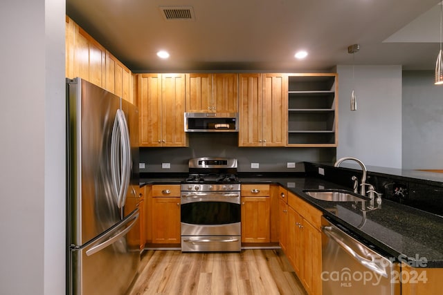 kitchen featuring decorative light fixtures, sink, light hardwood / wood-style flooring, appliances with stainless steel finishes, and dark stone counters