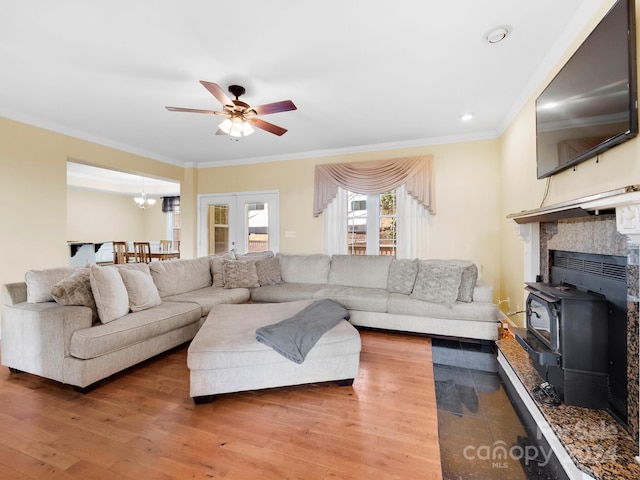 living room featuring french doors, a wood stove, crown molding, ceiling fan with notable chandelier, and hardwood / wood-style floors