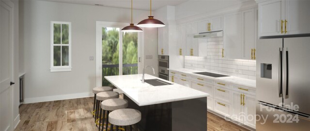 kitchen with an island with sink, stainless steel appliances, light hardwood / wood-style flooring, and backsplash