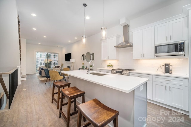 kitchen featuring decorative light fixtures, light hardwood / wood-style floors, stainless steel microwave, wall chimney exhaust hood, and sink