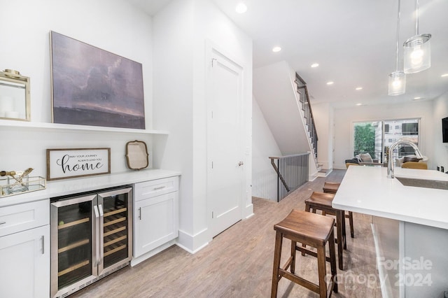 bar featuring decorative light fixtures, light hardwood / wood-style floors, wine cooler, white cabinets, and sink