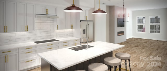 kitchen with sink, hanging light fixtures, light stone counters, high end white fridge, and a center island with sink