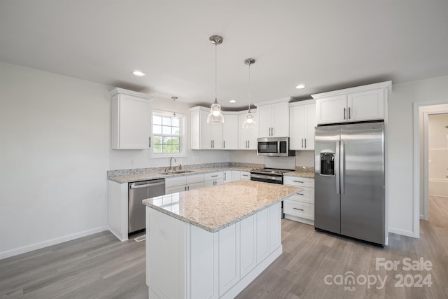 kitchen with appliances with stainless steel finishes, a kitchen island, light hardwood / wood-style floors, white cabinets, and pendant lighting