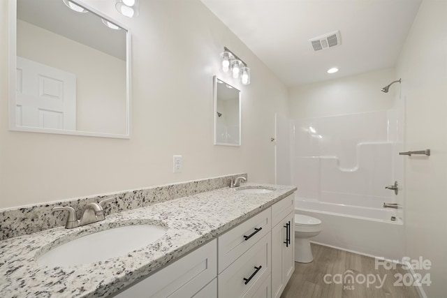 full bathroom with vanity with extensive cabinet space, washtub / shower combination, double sink, hardwood / wood-style flooring, and toilet