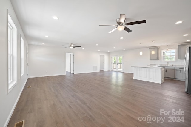 unfurnished living room featuring a healthy amount of sunlight, ceiling fan, and dark hardwood / wood-style flooring