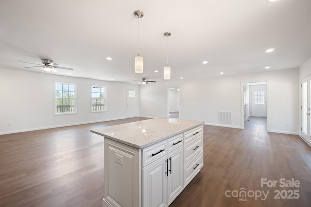 kitchen featuring light stone counters, decorative light fixtures, a kitchen island, white cabinetry, and dark hardwood / wood-style floors