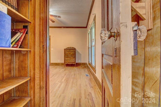 interior space featuring a textured ceiling, light hardwood / wood-style floors, and ornamental molding