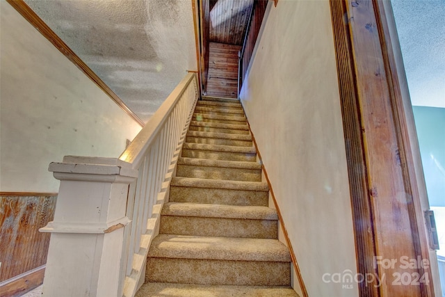 staircase with ornamental molding and a textured ceiling