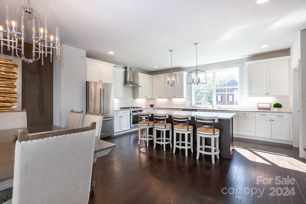 kitchen with premium appliances, a kitchen island, wall chimney range hood, and white cabinetry