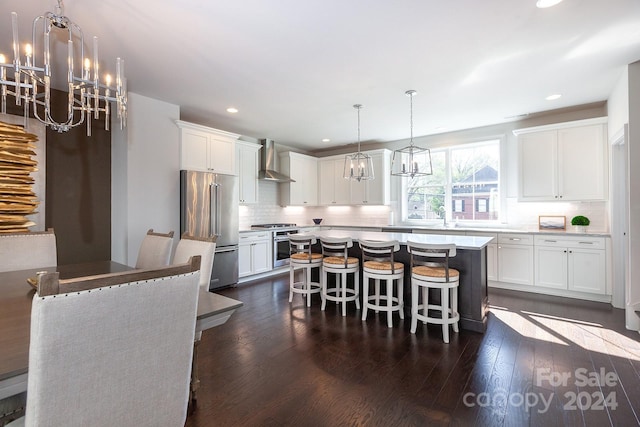 kitchen with premium appliances, a kitchen island, wall chimney range hood, and white cabinetry