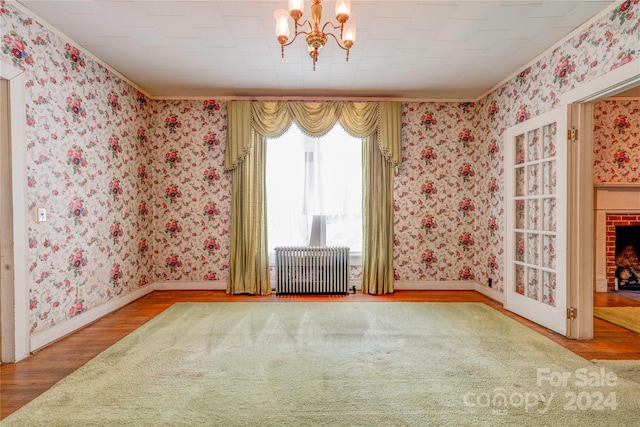 empty room with an inviting chandelier, radiator, and hardwood / wood-style floors