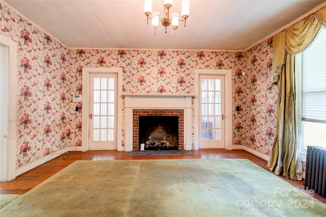 unfurnished living room with hardwood / wood-style floors, crown molding, radiator, and an inviting chandelier