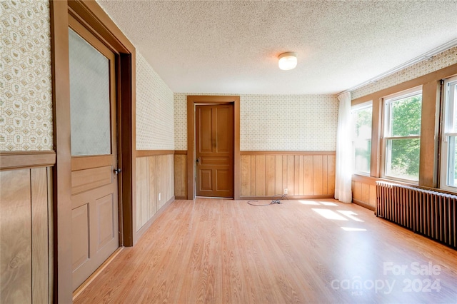 spare room with light hardwood / wood-style floors, radiator heating unit, and a textured ceiling