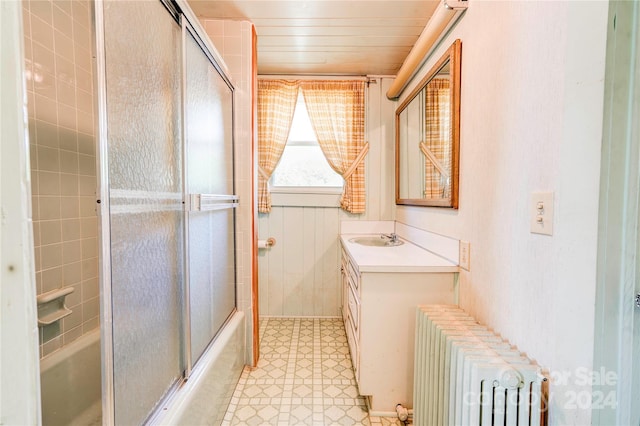 bathroom with vanity with extensive cabinet space, combined bath / shower with glass door, radiator heating unit, and tile flooring