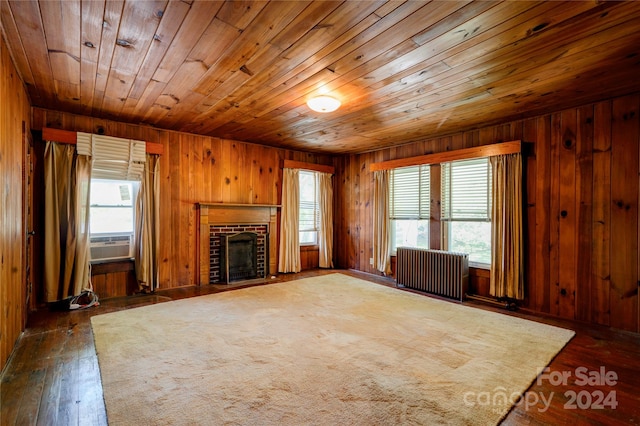 unfurnished living room with dark hardwood / wood-style flooring, wooden walls, radiator, and a fireplace