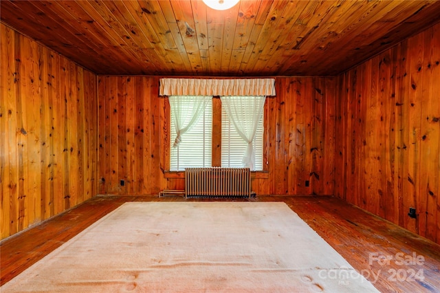 unfurnished room featuring wood walls, radiator, dark hardwood / wood-style floors, and wood ceiling