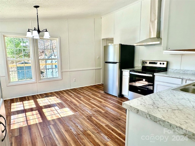 kitchen featuring pendant lighting, white cabinets, wall chimney range hood, stainless steel appliances, and a chandelier